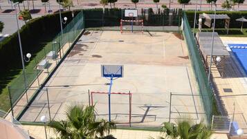 Een basketbalveld buiten met een net, omringd door een hek, en palmbomen op de voorgrond.