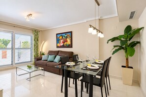 A modern living room with a glass dining table, a brown sofa, and a large potted plant.