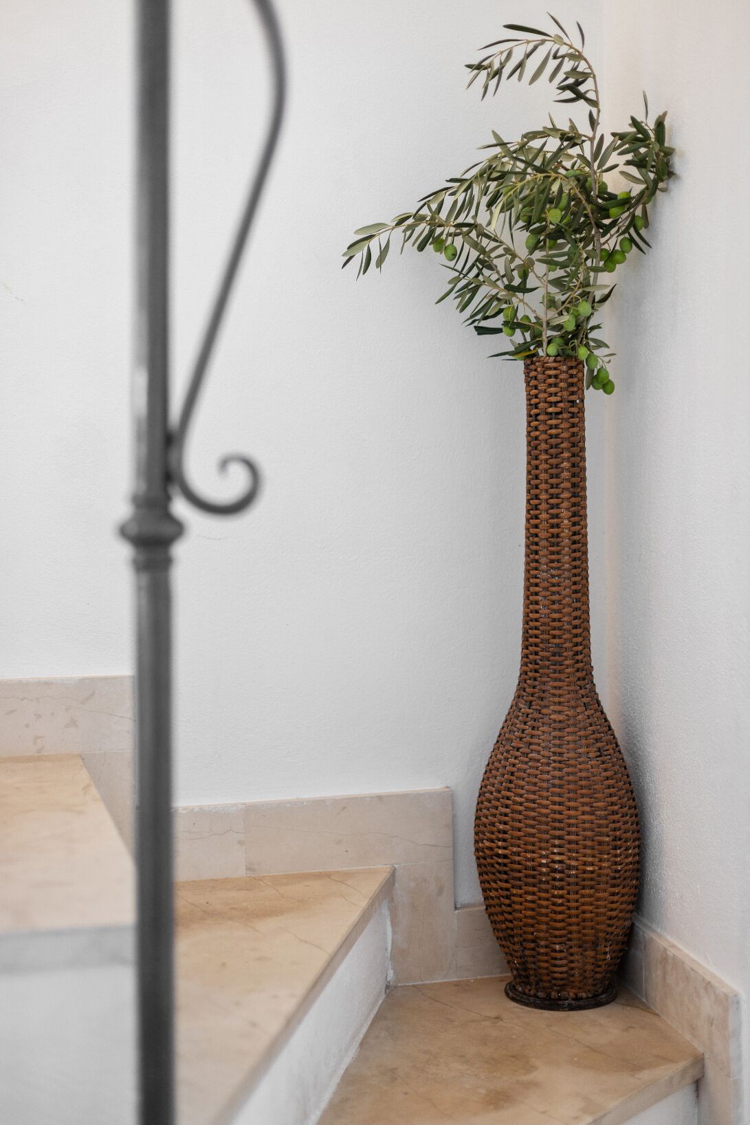 A tall, woven wicker vase with green foliage on a staircase.