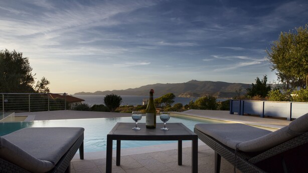 A poolside area with a table, two lounge chairs, and a bottle of wine. - Sea views in a tranquil area. Infinity saline pool. AC & WIFI (magomados)