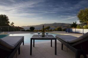 Un área junto a la piscina con una mesa, dos sillas reclinables y una botella de vino.