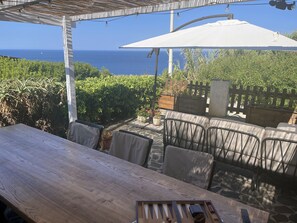 Una mesa de madera con sillas y un paraguas blanco en un patio al aire libre con vista al océano.