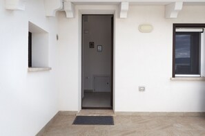 Un pasillo con una puerta que da a una habitación, un ventanal pequeño y una lámpara fijada a la pared.