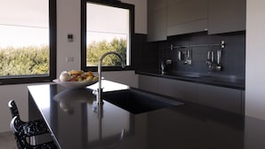 A modern kitchen with a large window, a bowl of fruit on the counter, and stainless steel appliances. - Sea views in a tranquil area. Infinity saline pool. AC & WIFI (magomados)