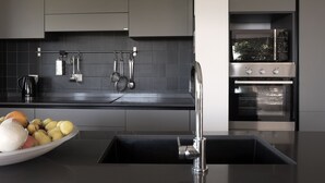 A modern kitchen with a black countertop, stainless steel appliances, and a variety of utensils hanging on the wall. - Sea views in a tranquil area. Infinity saline pool. AC & WIFI (magomados)