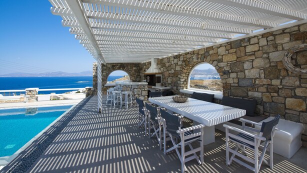 An outdoor dining area with stone walls, a pool, and a view of the sea. - Villa Orion Mykonos - Blue Views Mykonos Villas (Mykonos)