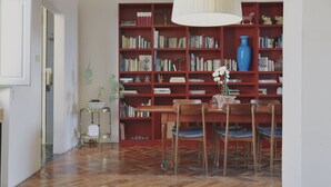 Ein Zimmer mit Holzboden, einem roten Bücherregal voller Bücher, einem Esstisch mit Stühlen und einer Hängelampe.