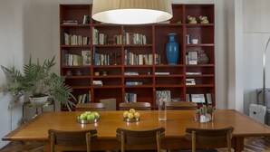 Ein Essbereich mit einem Holztisch, Stühlen, einem Bücherregal voller Bücher, einer Topfpflanze und einer Vase.