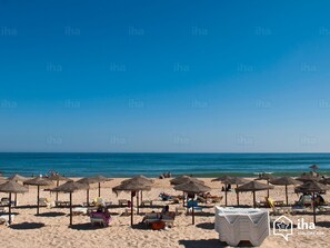 A beach with sun loungers and umbrellas, a clear sky, and the ocean in the background.