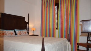 Una cama con cabecera de madera, una mesita de noche con lámpara y una silla.