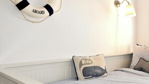 A bedroom with a striped bedspread, a life preserver decoration, a wall-mounted lamp, and a pillow with a whale design.