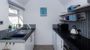 A modern kitchen with a black and white tiled backsplash, a blue sign on the wall, and a kettle on the counter.