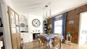 A dining area with a wooden table, chairs, a clock, and a brick wall.