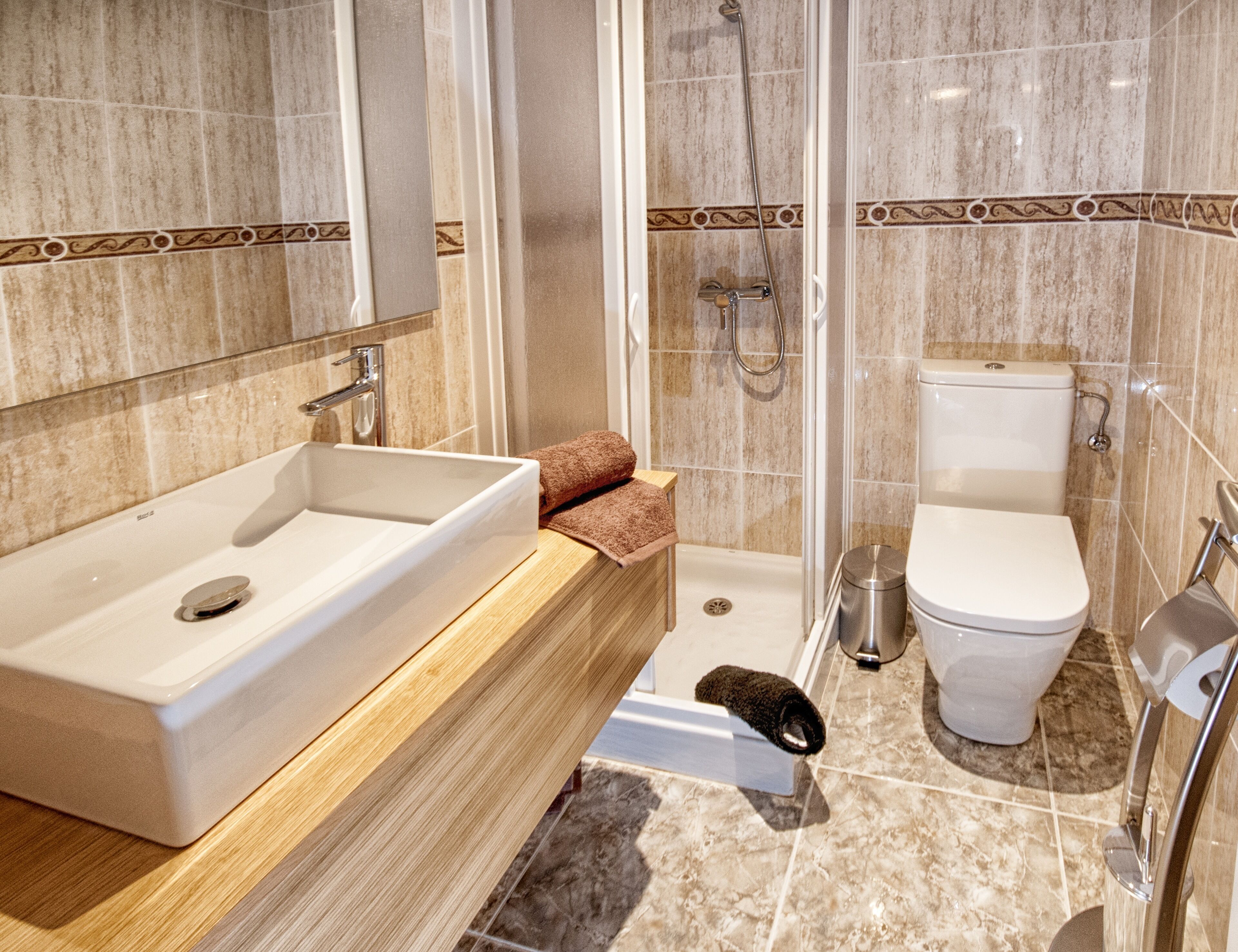 A modern bathroom with a large sink, a shower, and a toilet.