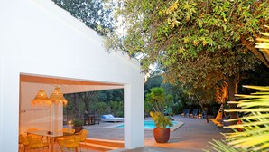 Uma área de varanda externa com mesa e cadeiras de vidro, piscina e espreguiçadeiras.