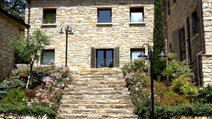 Ein Steinhaus mit einer Treppe, die zu einer Tür führt, umgeben von üppigen Gärten und Blumen.