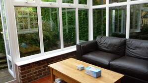 A conservatory with a black leather sofa and a wooden coffee table. - Brick and flint pet friendly cottage a short walk to sandy beach and pub (Holme next-the-sea)