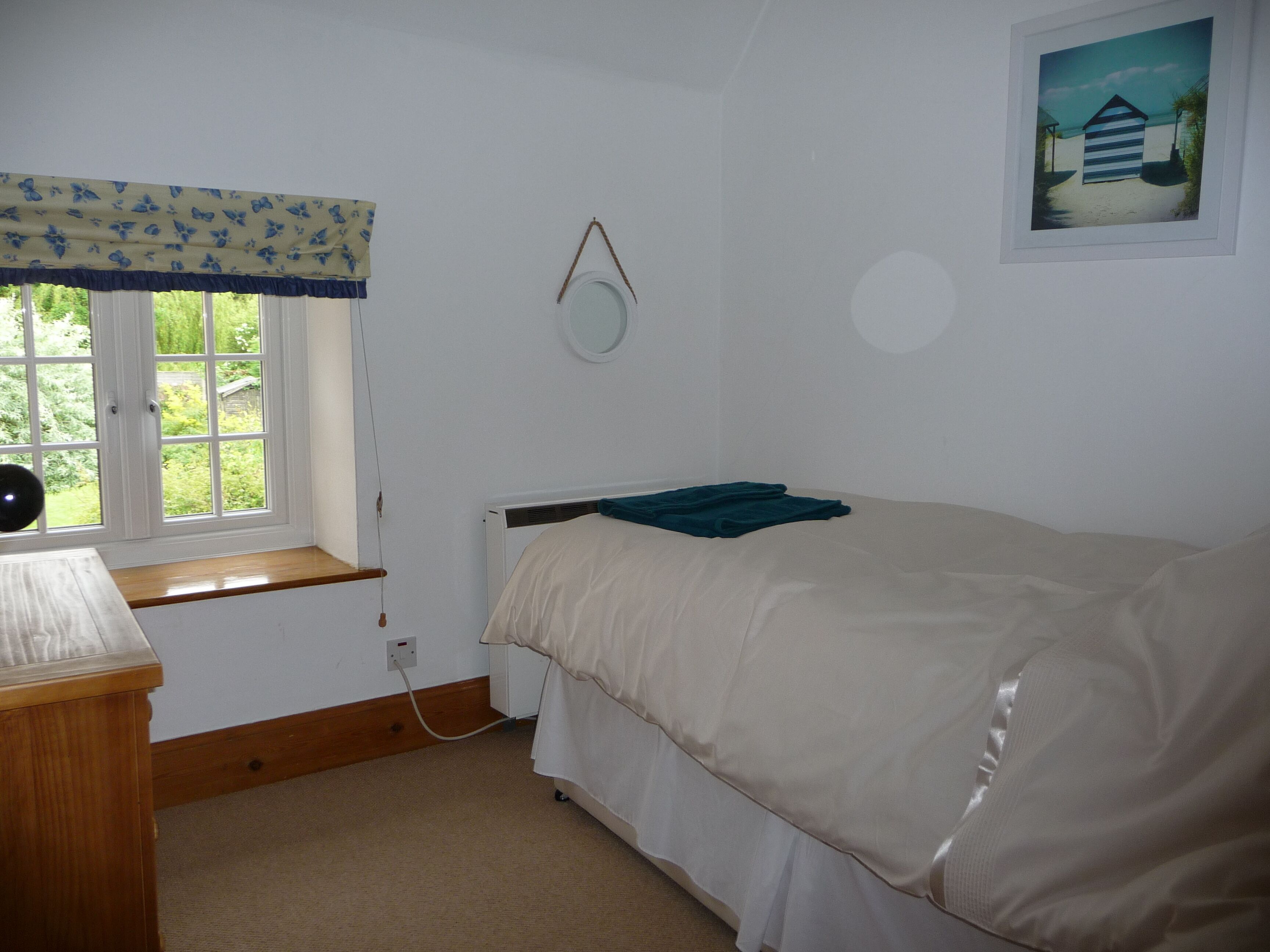 Un dormitorio con una cama individual, una ventana con cortina, una mesita de noche y un espejo colgado en la pared.