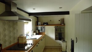 A compact kitchen with a wooden countertop, a built-in oven, and a microwave. - Brick and flint pet friendly cottage a short walk to sandy beach and pub (Holme next-the-sea)