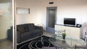 Una sala de estar moderna con un sofá, una mesa de vidrio, un televisor y una puerta.
