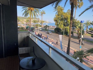 Un balcon donnant sur une rue animée, des palmiers et une côte lointaine.