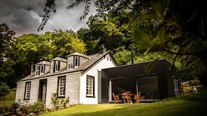 A two-story house with a large garage and a dining area with outdoor furniture. - Modern Cottage, big garden, AGA, Loch/Mountain Views. Cinema Room & Log Burner (Arrochar)