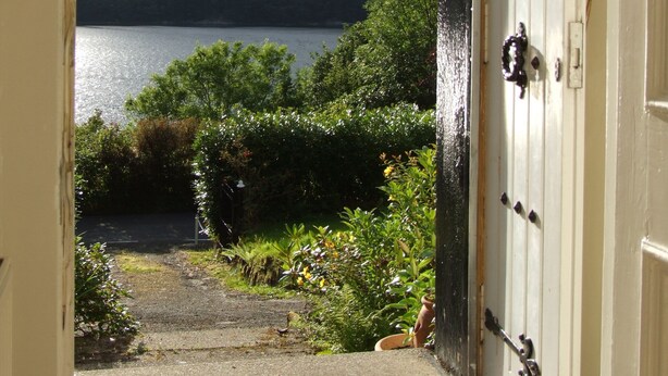 A view through an open door to a garden with a lake and mountains in the background. - Modern Cottage, big garden, AGA, Loch/Mountain Views. Cinema Room & Log Burner (Arrochar)