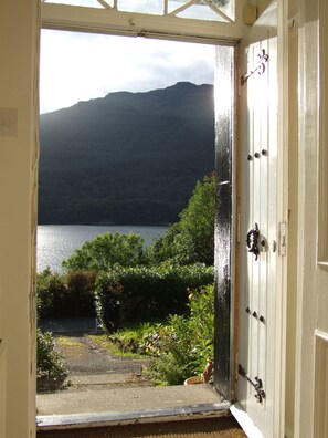 A view through an open door to a garden with a lake and mountains in the background. - Modern Cottage, big garden, AGA, Loch/Mountain Views. Cinema Room & Log Burner (Arrochar)