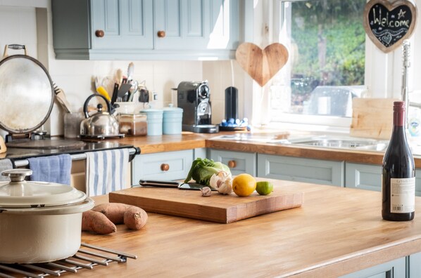 A kitchen counter with a cutting board, vegetables, a wine bottle, and a heart-shaped welcome sign. - Modern Cottage, big garden, AGA, Loch/Mountain Views. Cinema Room & Log Burner (Arrochar)