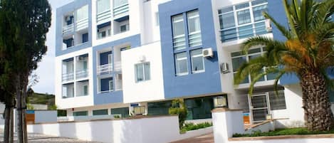 A modern multi-story building with balconies, air conditioning units, and a paved courtyard.