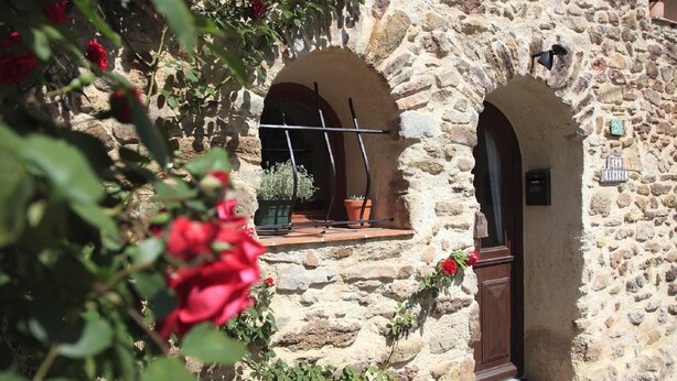 Um edifício de pedra com portais em arco e uma pequena varanda com plantas em vasos.