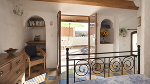 Quarto com cama, cômoda, cadeira de vime, estante e vista para o exterior.