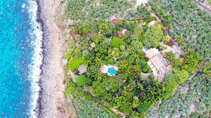 Vista aérea de una propiedad costera con piscina, varias edificaciones y abundante vegetación.