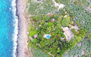 Vista aérea de una propiedad costera con piscina, varias edificaciones y abundante vegetación.