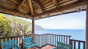 Terraza de madera con dos sillas azules y barandilla de madera, con vista a un cuerpo de agua.