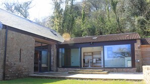 Ein modernes Haus mit Naturstein-Fassade, großen Glasfenstern und einer Terrasse.