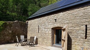 Ein Steinhaus mit Holztür, einem Tisch mit Stühlen und einem Solarmodul auf dem Dach.