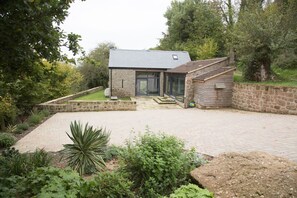 A modern house with a stone exterior, a paved driveway, and a garden with various plants. - Beautiful "ECO" barn conversion in Wye Valley - ideal for couples plus two kids (Penallt)