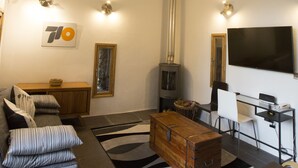 Ein großzügiger Wohnbereich mit hoher Decke, Holzbalken, Kamin, einer Couch, einem Couchtisch und einem Flachbildfernseher.