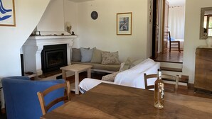 Ett vardagsrum med en öppen spis, en soffa, ett matbord och en blå fåtölj.