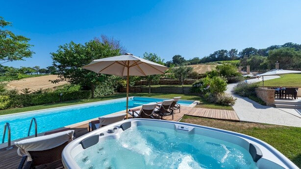 Un bain à remous avec une terrasse en bois et des chaises longues, une piscine et un espace patio équipé d’un parasol.