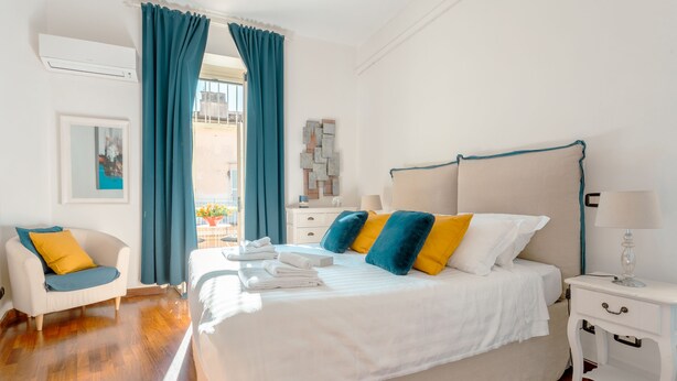 A hotel room with a large bed, a bedside table, a chair, and a view of the outside. - PIAZZA DI SPAGNA APARTMENT (Roma)