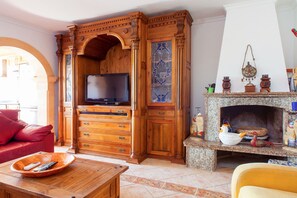 A living room with a wooden cabinet, a television, a fireplace with decorative items, and a red sofa. - Beautiful villa Ramos in San Antonio Bay with BBQ and large pool (Sant Josep de Sa Talaia / San Jose)