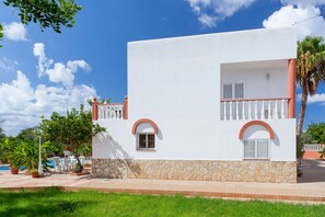 A white building with stone base, two windows with shutters, and a balcony with a railing.
