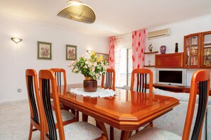 A dining room with a wooden table, six chairs, a vase of flowers, and a television on a stand. - Beautiful villa Ramos in San Antonio Bay with BBQ and large pool (Sant Josep de Sa Talaia / San Jose)