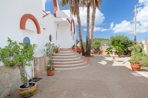 Un bâtiment blanc orné d’arcs rouges, avec un escalier en pierre et des plantes en pot.