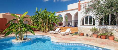 Ein Poolbereich mit Liegestühlen, einer Palme und einem Gebäude mit Bögen.