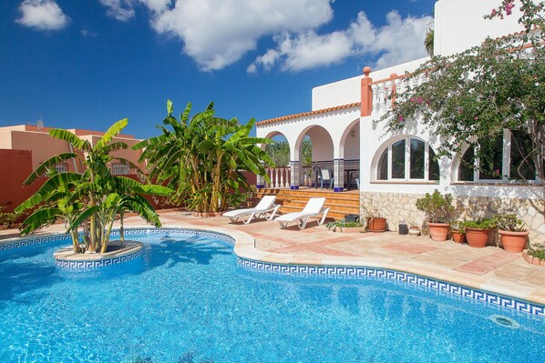 A pool area with lounge chairs, a palm tree, and a building with arches.