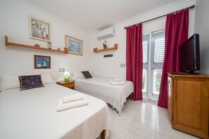 A hotel room with two beds, a television, a window with curtains, and artwork on the walls.