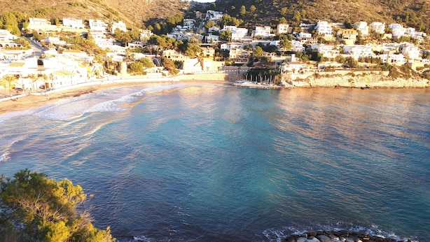 Un pueblo costero con edificios blancos, un litoral rocoso y un mar azul cristalino.